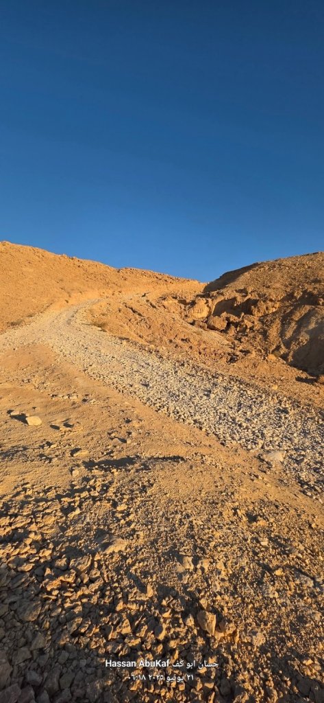صورة تظهر مساراً وعرًا يصعد إلى قمة جبل في منطقة صحراوية تحت سماء صافية.