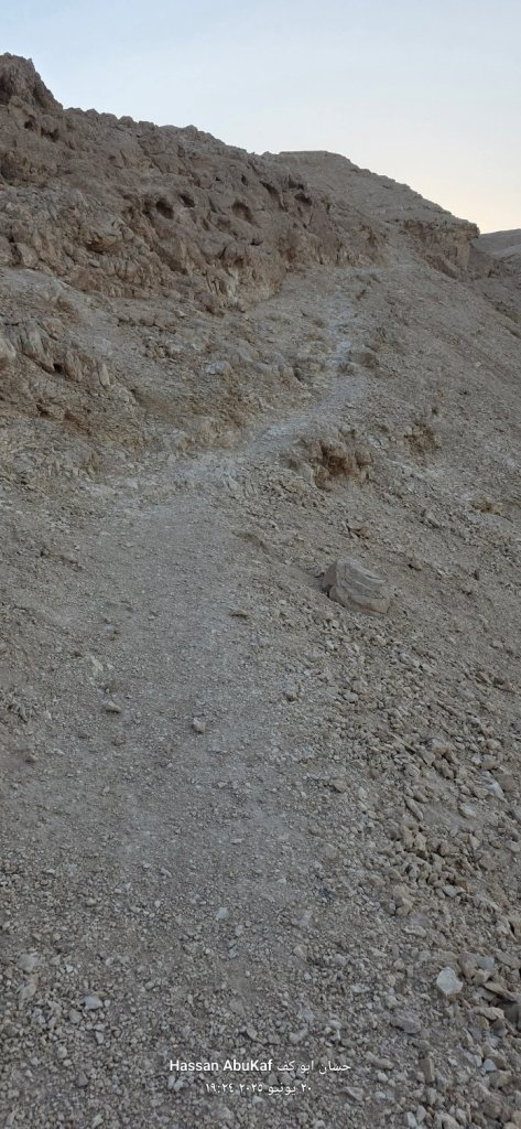 مسار صخري ضيق يتجه لأعلى على جبل، مع تدرجات صخرية واضحة في المناظر الطبيعية، يُظهر التضاريس الصحراوية القاحلة.